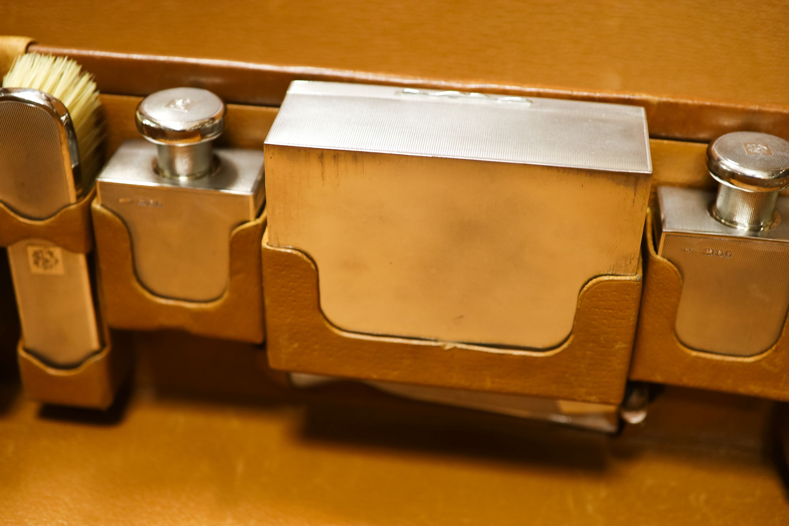 A 1930's Harrods pigskin travelling toilet case with seven engine turned silver fittings, including brushes, cigarette box and two scent bottles, F & Co Ltd, London, 1933, case 66.5cm.